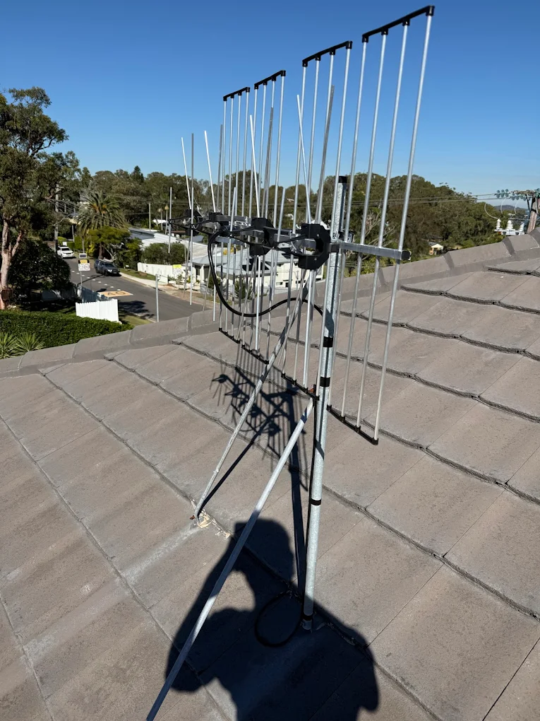 TV antenna mounted on a tiled rooftop with clear blue skies